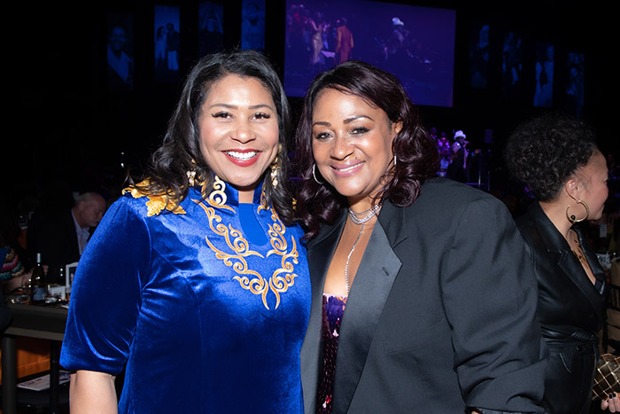 San Francisco Mayor London Breed, in a blue-and-gold evening dress, poses with GLIDE CEO and President Dr. Gina Fromer, in a purple evening dress with a gray overcoat.