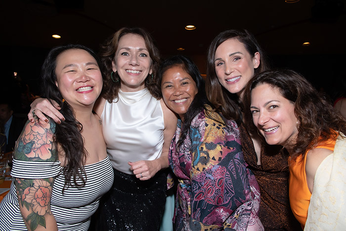 Five smiling women in evening clothes group together for a picture as Jam partygoers.