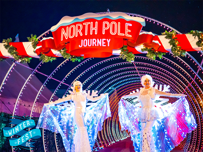 Two dancers in gauzy costumes welcome visitors to a lighted archway with a red sign that advertises, "North Pole Journey".