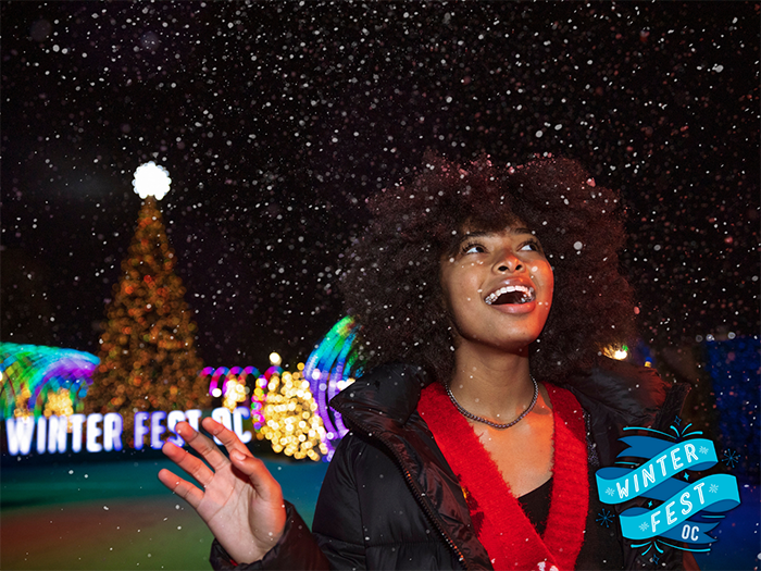 Young girl smiles and looks amazed as "snow" falls, with a Christmas tree in the background.