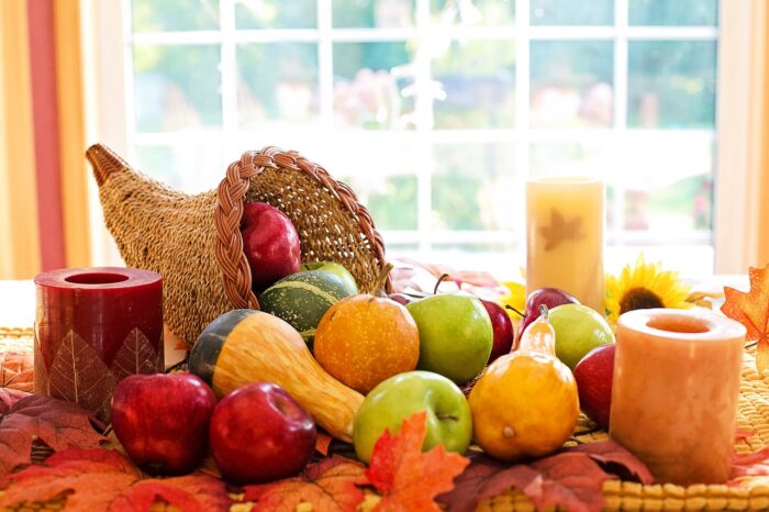 REattan cornucopia by a window, overflowing with oranges and apples and surrounded by candles