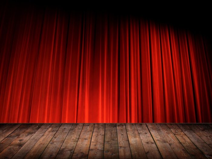 Red, backlit curtain down on a wooden stage.