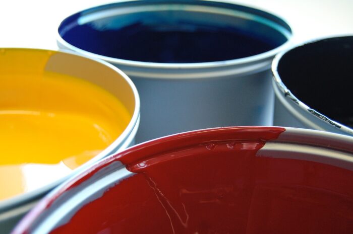 Four vats of silkscreening ink: red, yellow, blue, and a fourth rim with indeterminate color.