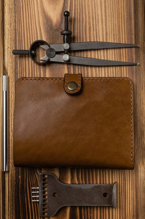 Leather wallet on wooden workbench with leather-carving tool.