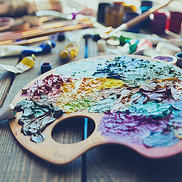 Artist's palette with a myriad of colors on it: turquoise, yellow, purple and green--against a studio background.