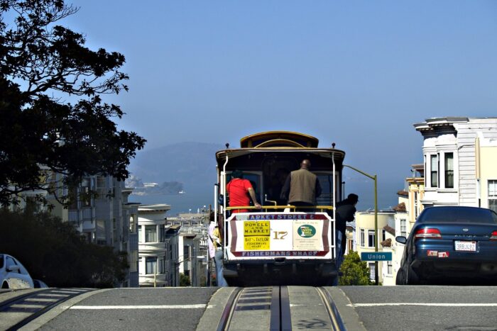 Cable car with passengers atop a San Francisco hill with Victorian houses.