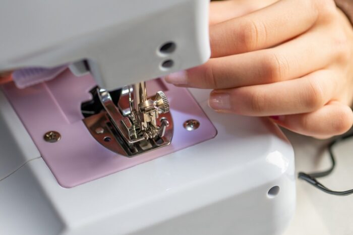 Closeup of a woman's hands, with pink nail polish, at a white sewing machine.