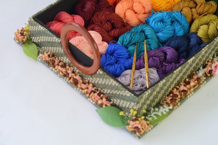 Square basket of a dozen skeins of yarn in different colors--blue, pink, rust, gray, brown, orange--with two crochet hooks.