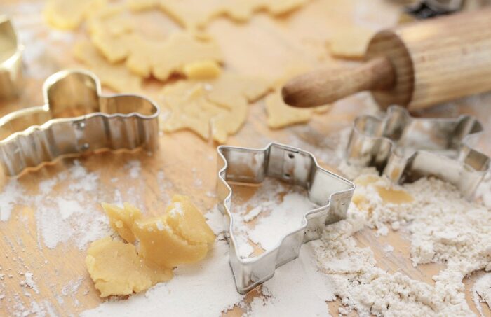 Sugar cooky dough on floured board with rolling pin and Christmas tree, gingerbread man and reindeer-shaped metal cooky cutters