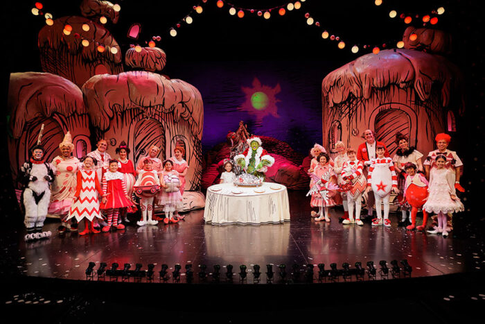 "The Grinch" onstage, surrounded by festive Whos and their fantastical houses.