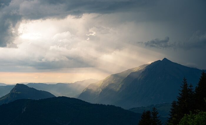 Light breaks through clouds and streams to earth over a mountain range.