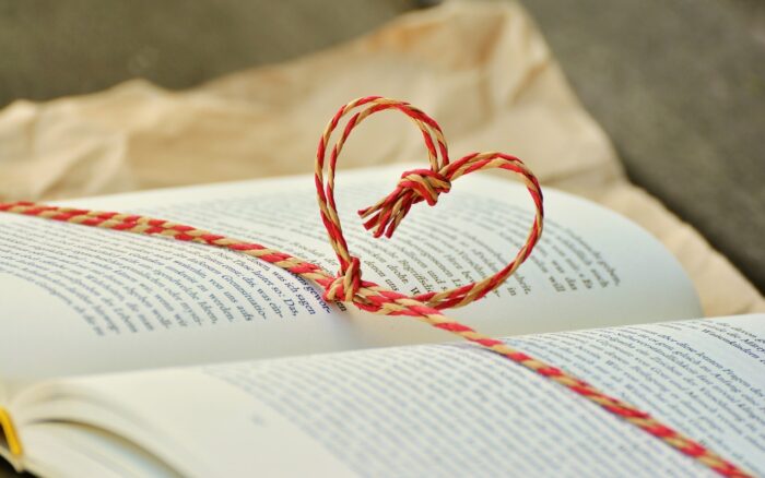 Open book agains brown wrapping paper with red-and-white cord, tied in aheart, across the pages.