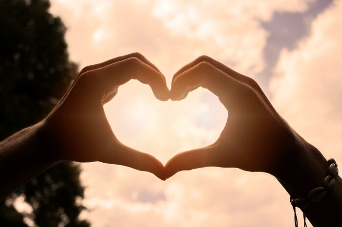 Two hands form a heart against a pink-lit background