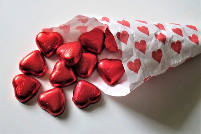 Foil-wrapped chocolate hearts spill out of a white paper cone printed with red hearts.