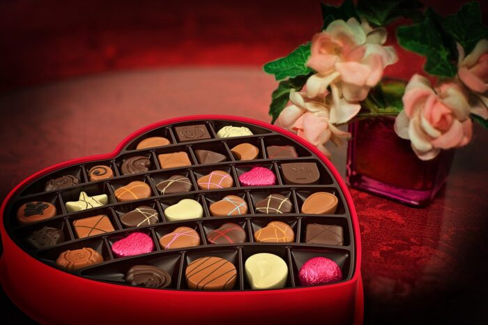 Heart-shaped box of Valentine chocolates next to pink roses.