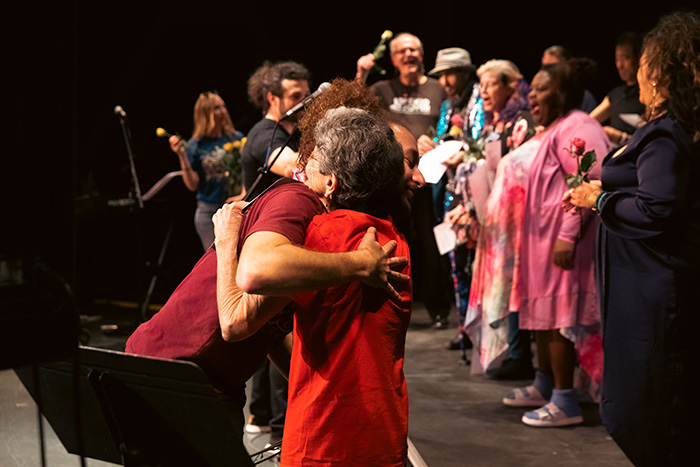 Two women hug near stage as choir sings
