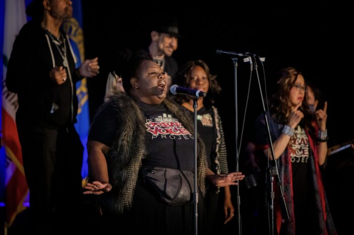 Closeup of soloist as she sings onstage, with choir behind her