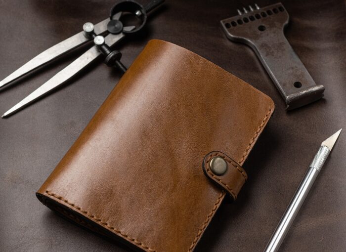 Leather hand-tooled wallet lies on a leatherworker's table with tools around it.