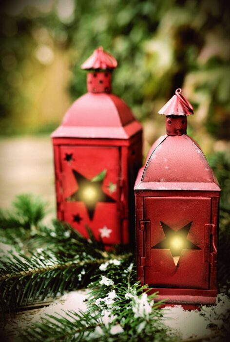 Two red tin lanterns with starshaped openings glow with white candles inside as they sit on a bed of pine branches.
