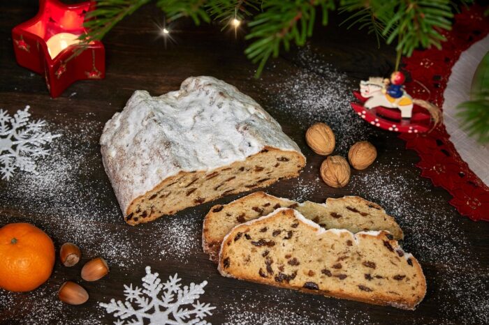 German iced stollen slices next to white snowflakes, a red star candle and a small wooden Christmas ornament of a child on a rocking horse