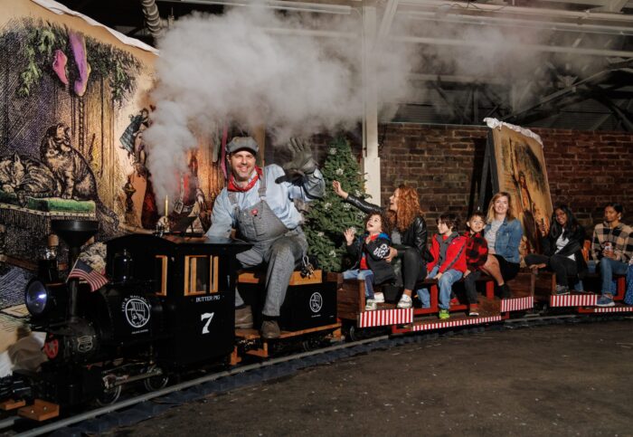 Miniature steam train with smiling Dickens Fair attendees aboard