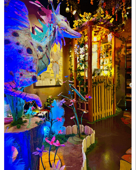 Enchanted forest ticket booth lit by gold lights, with a dragon, in blue lights, nearby.