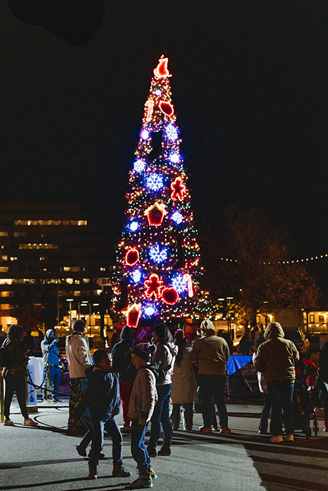 60-foot-tall Sacramento Christmas tree, lighted, stands against the night sky as shoppers admire it.
