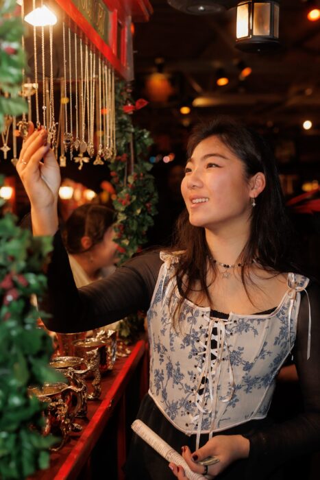 Smiling young Asian woman examines a gold necklace hanging from a display.