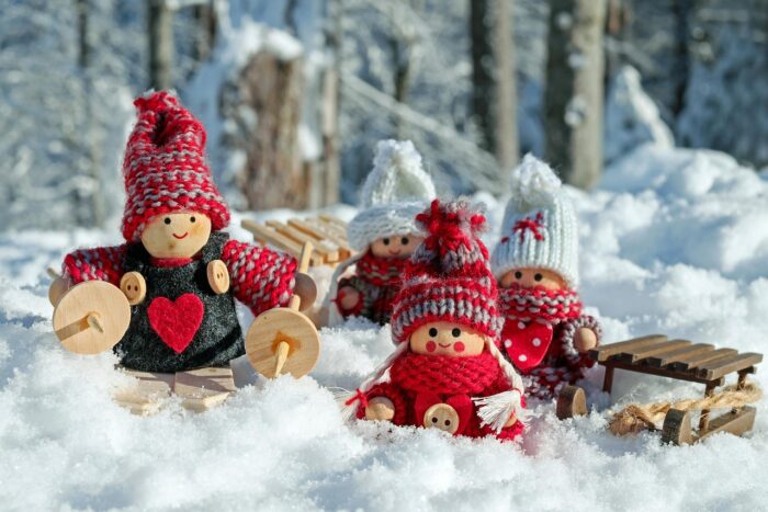 Two small Danish wooden dolls, with knitted caps and red felt hearts on their clothing, sit near wooden sleds amid cotton "snow"