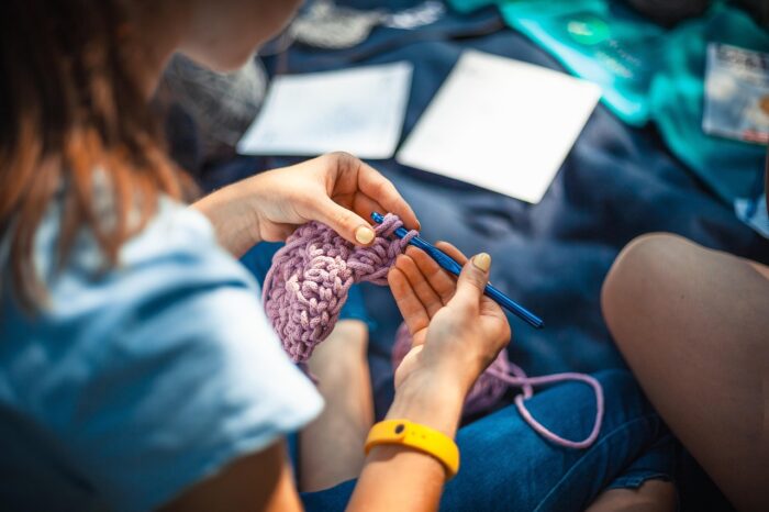 Closeup of young woman's hands as she pulls a crochet hook through a stitch on her rose-pink crocheting project.