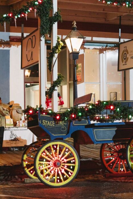 Blue stagecoach with gold wheels and a garland of greens and lights stands outside Stage Nine.