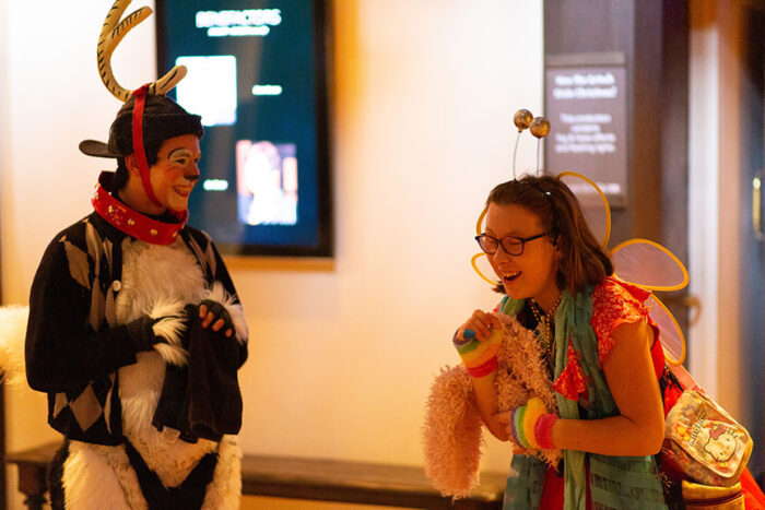 Young girl in a fairy costume laughs as she sees cast member dressed as Max as a reindeer, with a red nose and antlers.