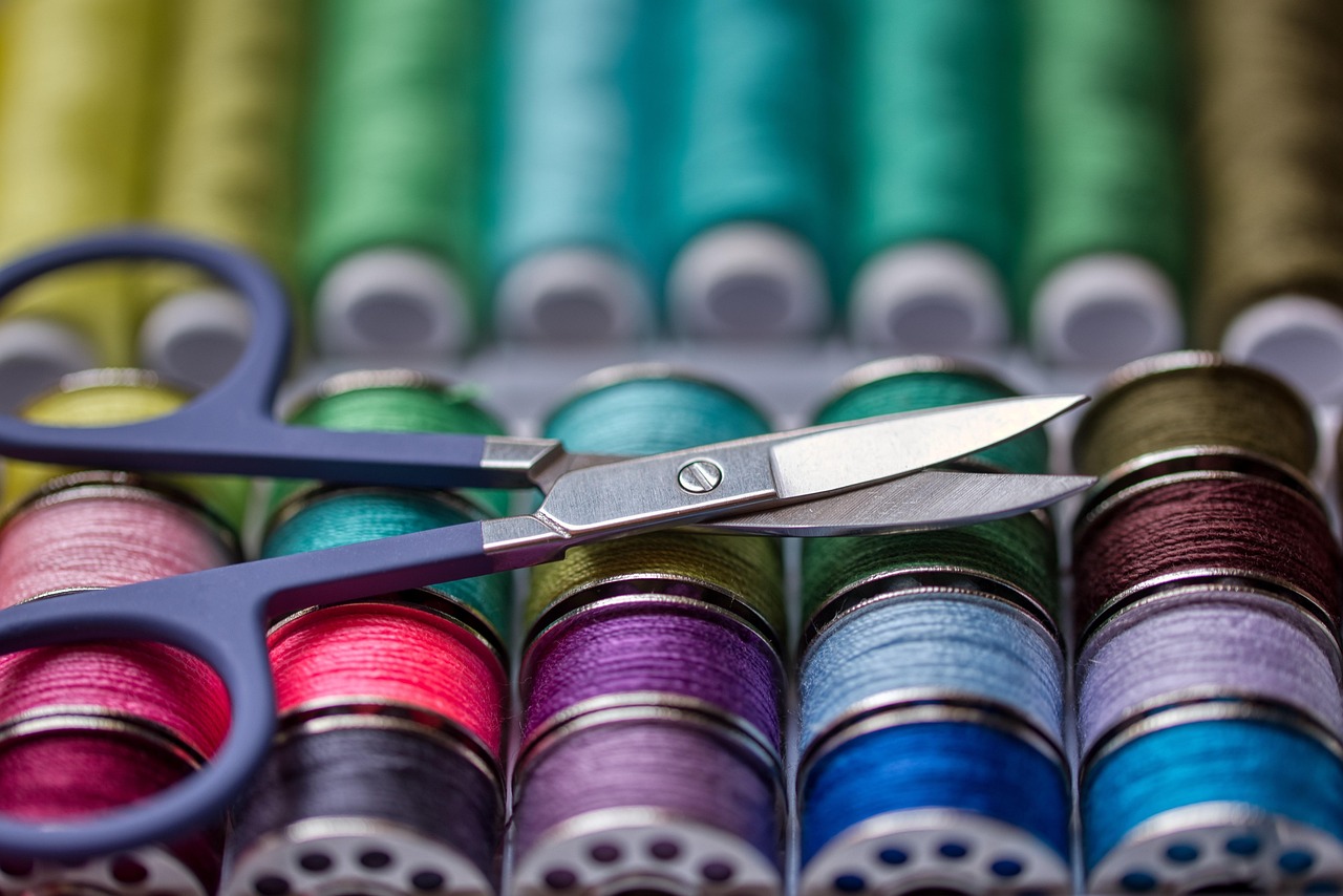 Bobbins on multicolored thread, mainly blues, greens and aqua with one red, one black and two purple, on top of which a small pair of embroidery scissors are sitting.