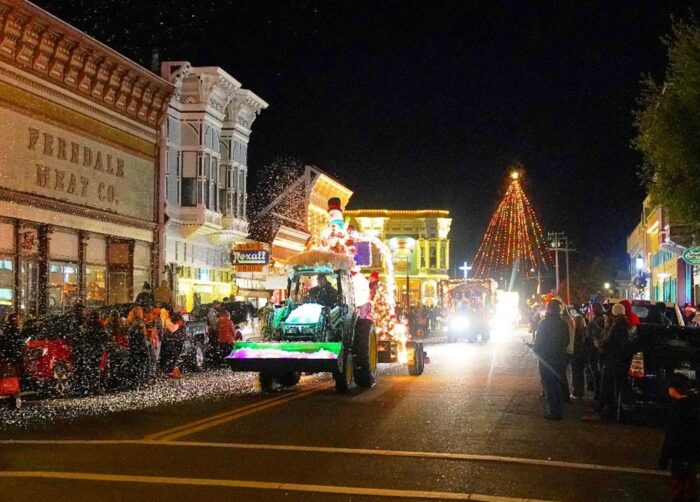 Lighted green John Deere tractor drives down Ferndale's Main Street, with tall lighted Christmas tree in the background.