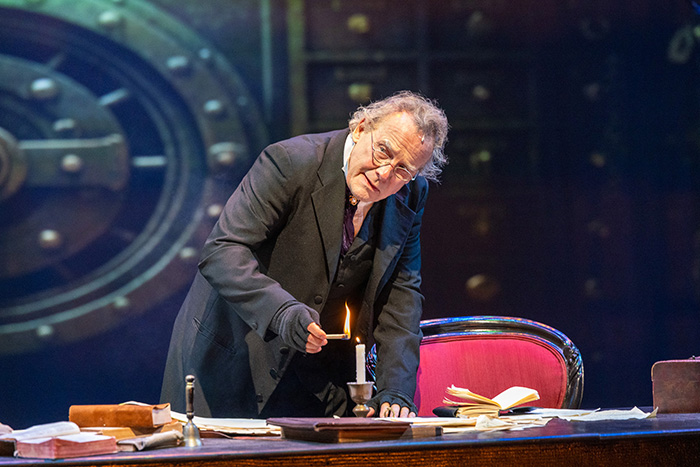 Geoff Elliot, as Scrooge, looks around as he lights a candle.