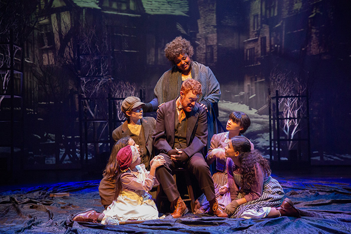 A downcast Bob Cratchit sits surrounded by his family.
