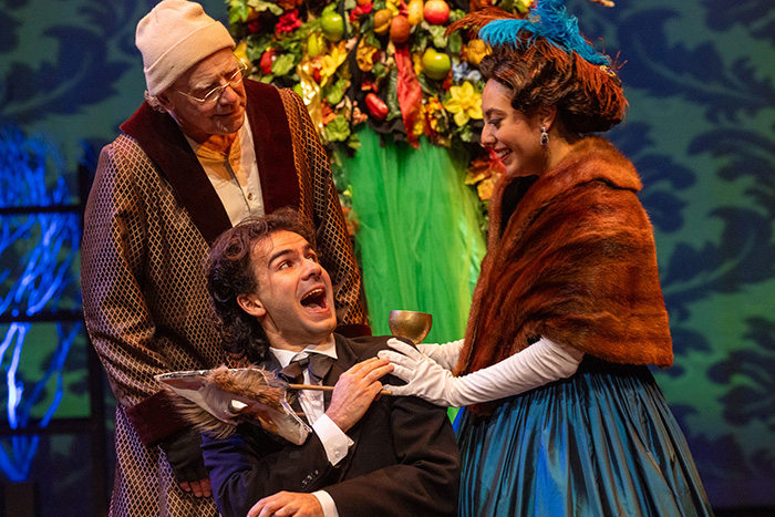 Scrooge watches his younger self court "Belle" against a background of a flowered arch.