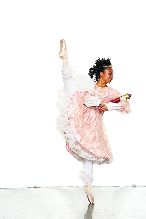 Clara, in a pink ruffled gown with petticoats, cradles the nutcracker in her arms as she balances en pointe.