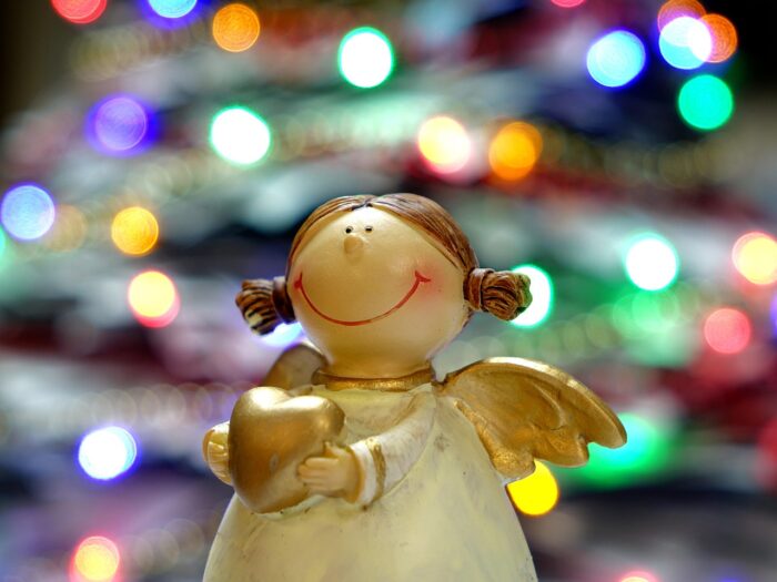 Small wooden angel in a white robe smiles and extends a gold heart.