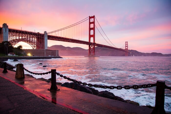 Golden Gate Bridge in distance against pink clouds with ocean in the forefront.