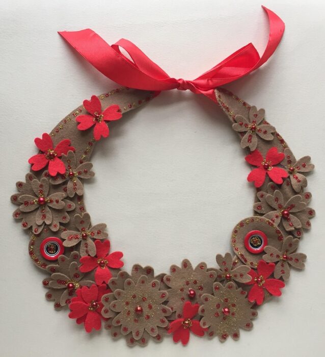 Wreath necklace made of brown felt with red flowers and beads and a red bow at the top.