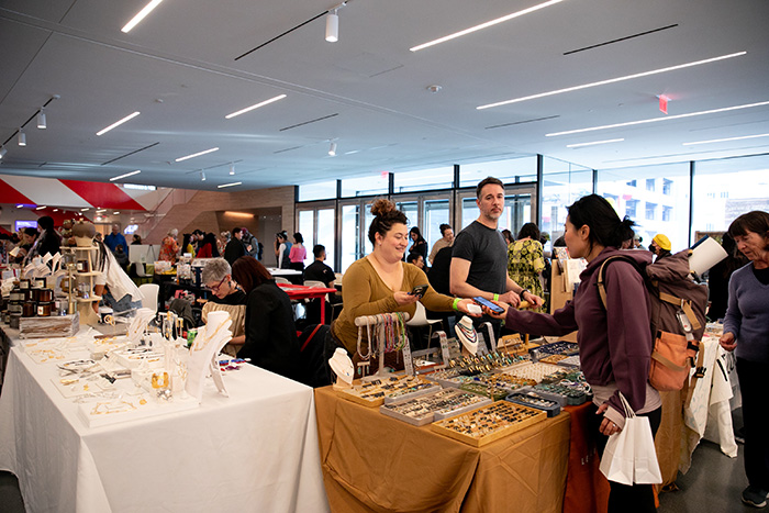 Smiling woman and man examine gold handcrafted jewelry at a table at SFMOMA Makers Market