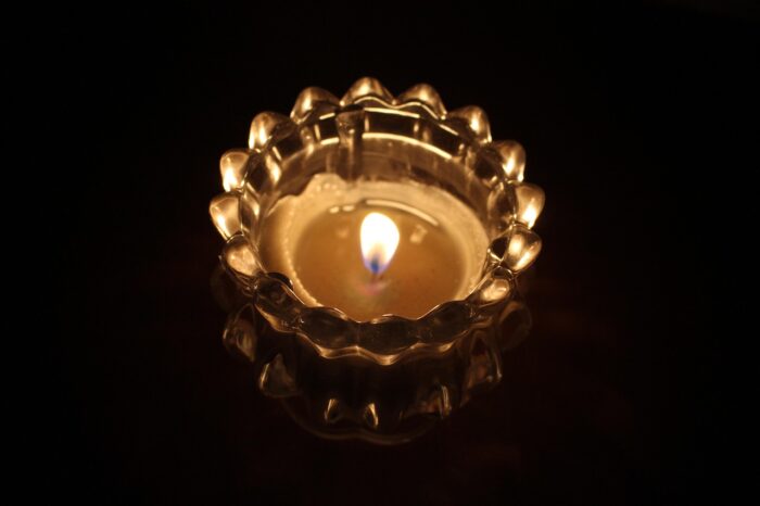 Gold candle with gold filagree glows against a dark background.