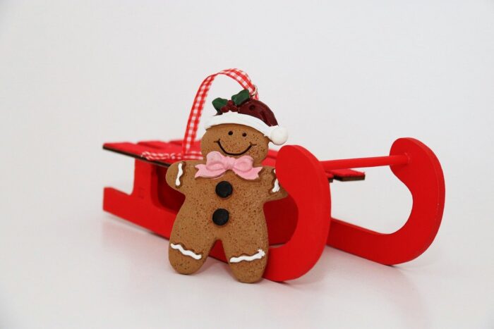 Smiling gingerbread ornament in a Santa cap against a red sled