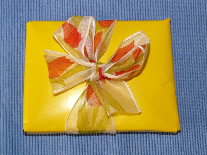 Flat yellow package with an orange-and-yellow ribbon on a blue cloth background