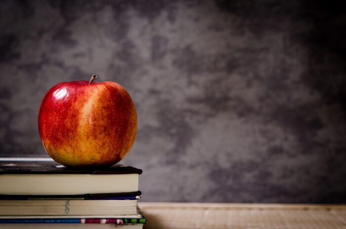 Red apple atop a stack of textbooks in front of a blackboard
