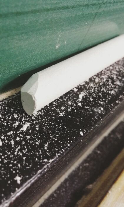 White chalk and chalk dust in the well of a green blackboard