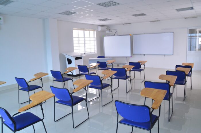 Blue chairs sit next to individual desks in a classroom with a whiteboard at the front