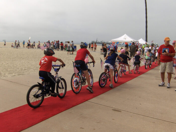Children on decorated bikes ride onto red carpet leading to the bike path