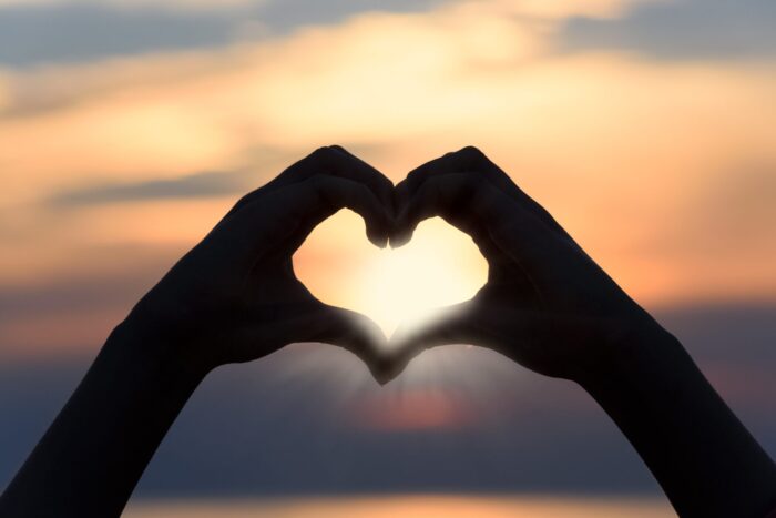 Two hands form a heart shape against a sunrise sky